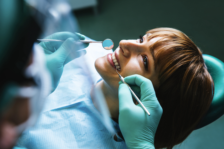 Femme allongée dans une chaise de dentiste avec un profesionnel qui tient des outils en regardant ses dents